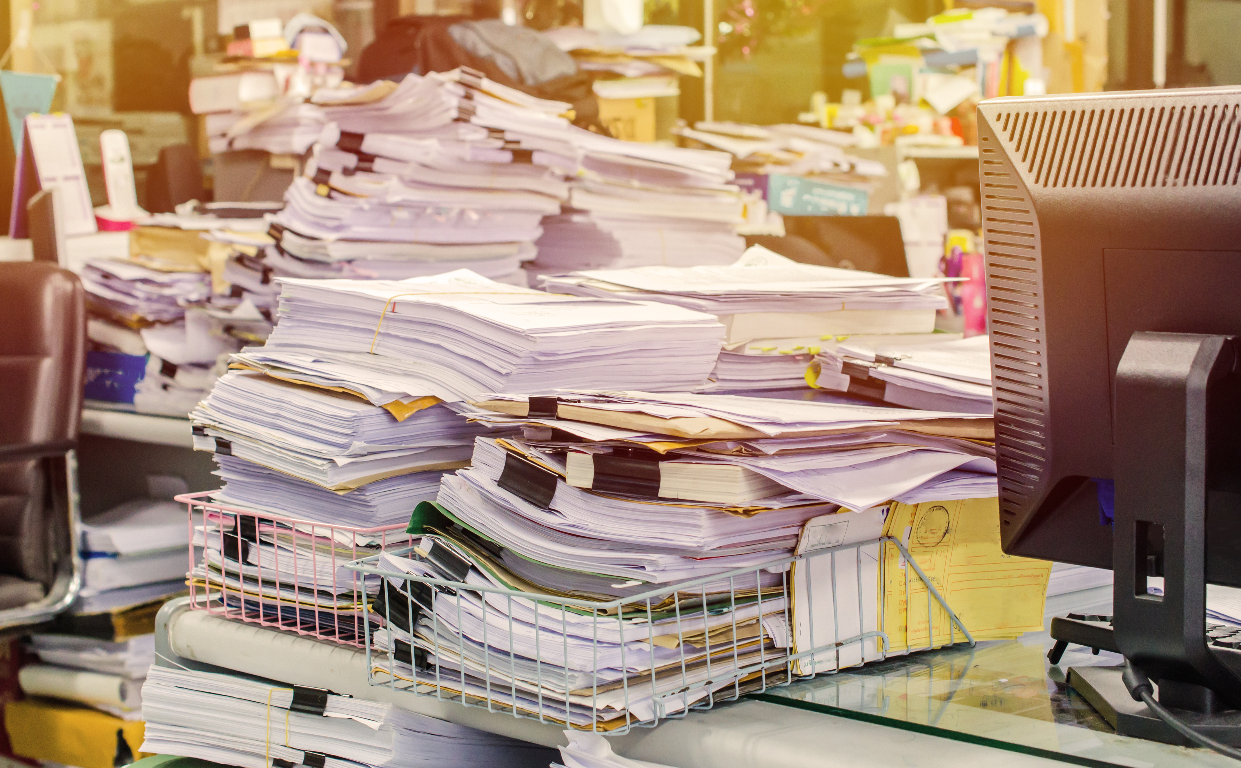 Pile of documents on desk stack up high waiting to be managed.